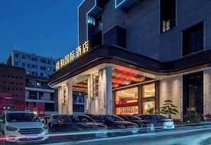 Un hotel con fachada moderna, fila de coches estacionados y una entrada visible.