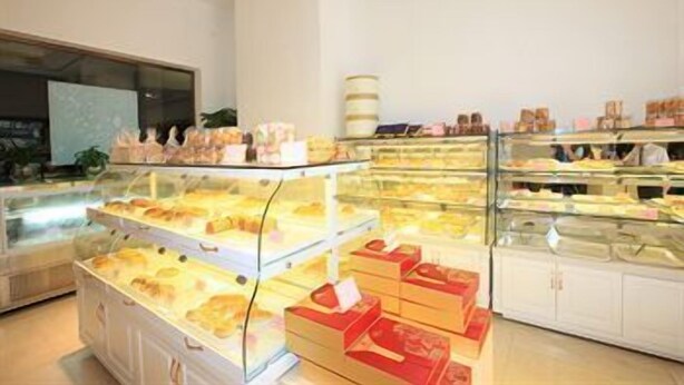 Mostrador de panadería con pasteles y pan, una barra repleta de productos horneados y un interior en tonos blancos.