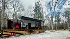 Eine rustikale Holzhütte mit einer Holzterrasse, einem überdachten Sitzbereich und einer Schotterzufahrt.