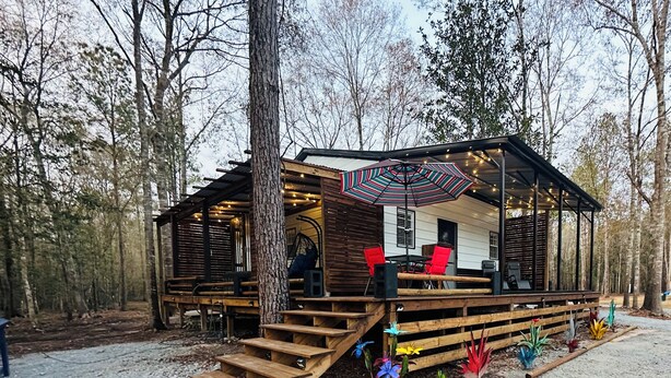 Eine Holzhütte mit einer überdachten Terrasse, Sitzgelegenheiten im Freien und einem kleinen Garten.