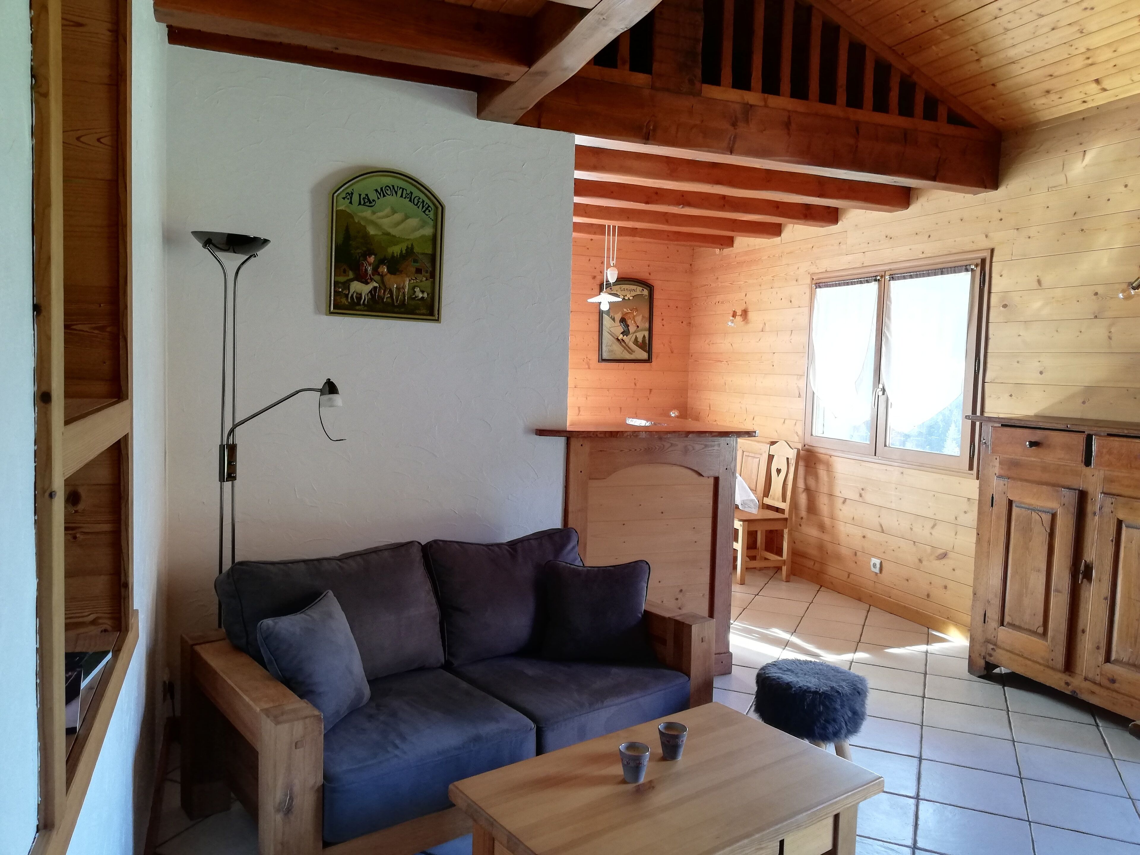 A cozy cabin interior with a wooden ceiling, a sofa, a table with cups, and a painting on the wall.