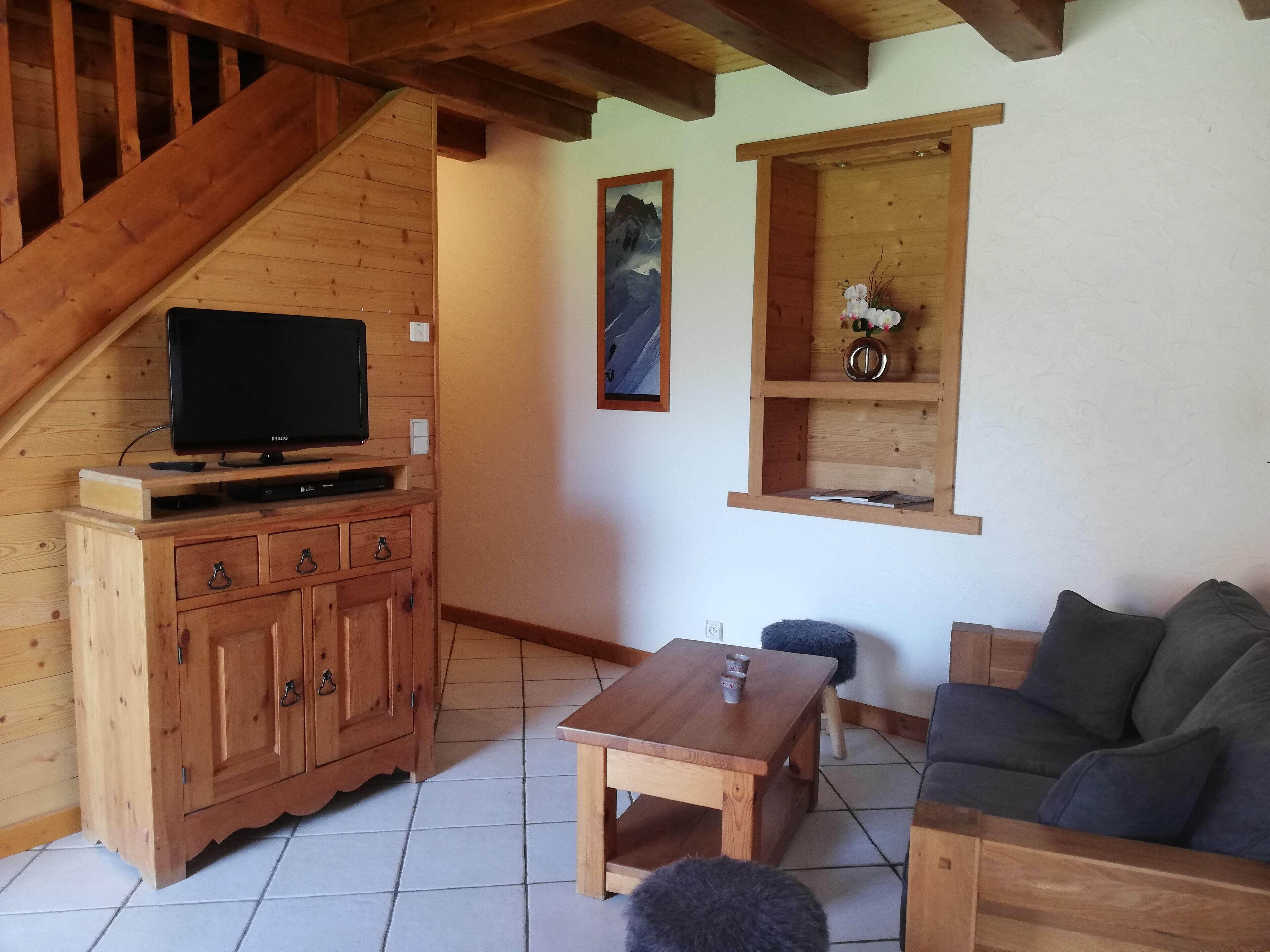 Un intérieur en bois avec une télévision posée sur un meuble, un canapé, une table et une fenêtre avec une étagère.