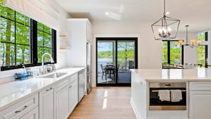 A modern kitchen with white cabinetry, a large island, and a view to an outdoor deck. - Lakefront Lake Anna 5 Suites, Dock, Hot Tub (Spotsylvania Courthouse)