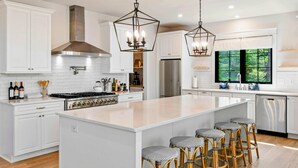 A modern kitchen with white cabinetry, a large island, bar stools, and a stainless steel refrigerator. - Lakefront Lake Anna 5 Suites, Dock, Hot Tub (Spotsylvania Courthouse)
