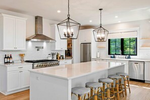 A modern kitchen with white cabinetry, a large island with bar stools, stainless steel appliances, and pendant lighting. - Lakefront Lake Anna 5 Suites, Dock, Hot Tub (Spotsylvania Courthouse)
