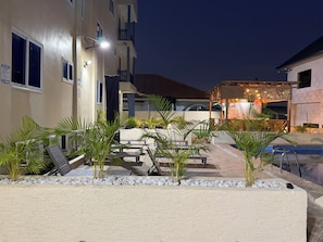 A hotel courtyard with outdoor seating, a pool, and a covered area with ambient lighting.