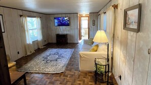 A cozy room with wooden floors, a sofa, a TV, and a lamp. - Escape to Comfort Near Higgins Lake! (Roscommon)