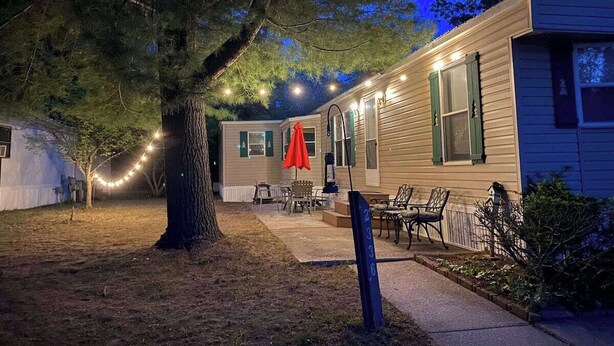 A two-story house with a covered patio, string lights, and a red umbrella. - Escape to Comfort Near Higgins Lake! (Roscommon)