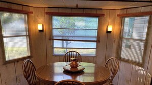 A round wooden table with four chairs, a central decorative item, and two wall-mounted lights. - Escape to Comfort Near Higgins Lake! (Roscommon)