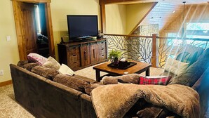A cozy living room with a sectional sofa, a flat-screen TV on a wooden stand, a coffee table with a plant, and a staircase leading to an upper level. - Luxury Lodge Retreat in the Heart of Suncadia – Walk to Golf, Winery & Trails (Cle Elum)