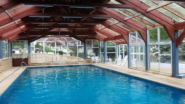 Una piscina interior con techo de cristal, rodeada de sillones de descanso y vistas al exterior.