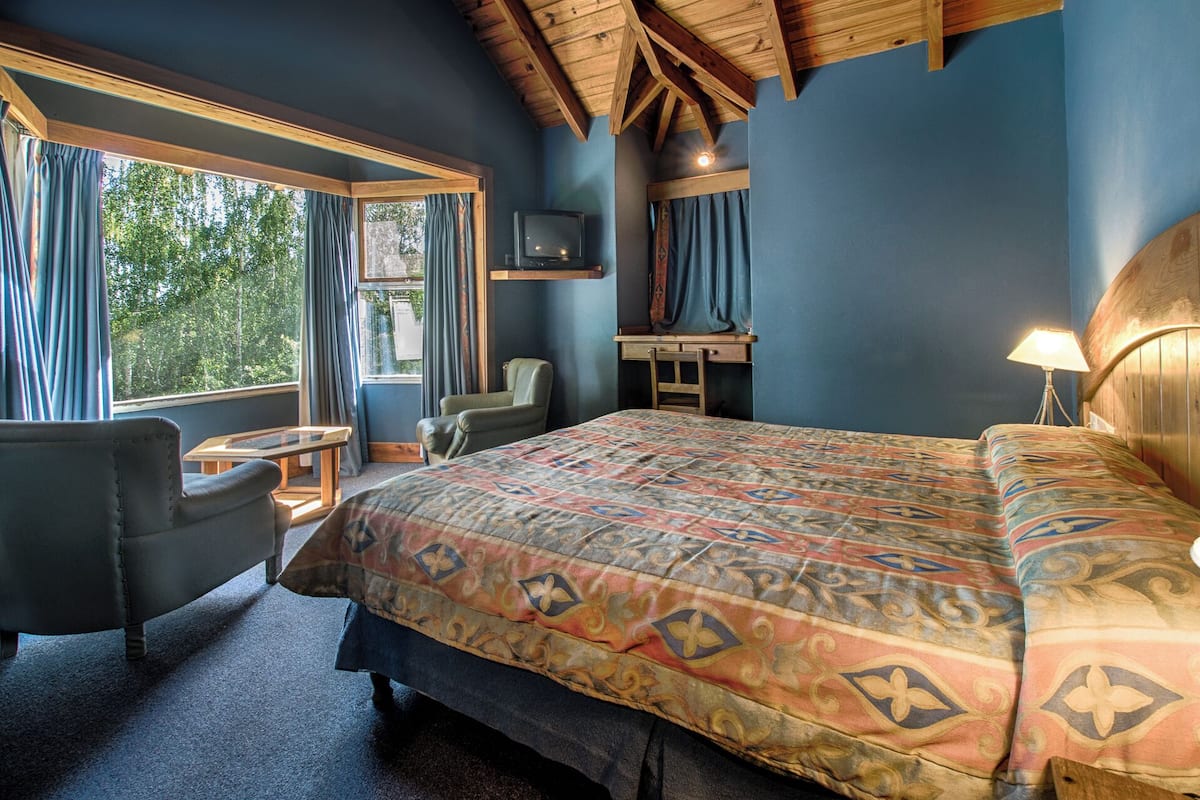 A bedroom with a large bed, a desk, a chair, and a television.