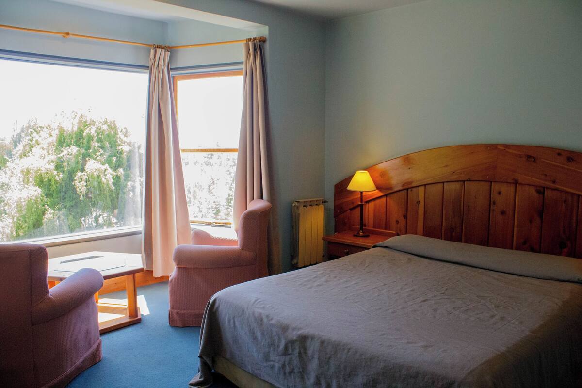 A bedroom with a bed, a chair, a table, and a window with curtains.