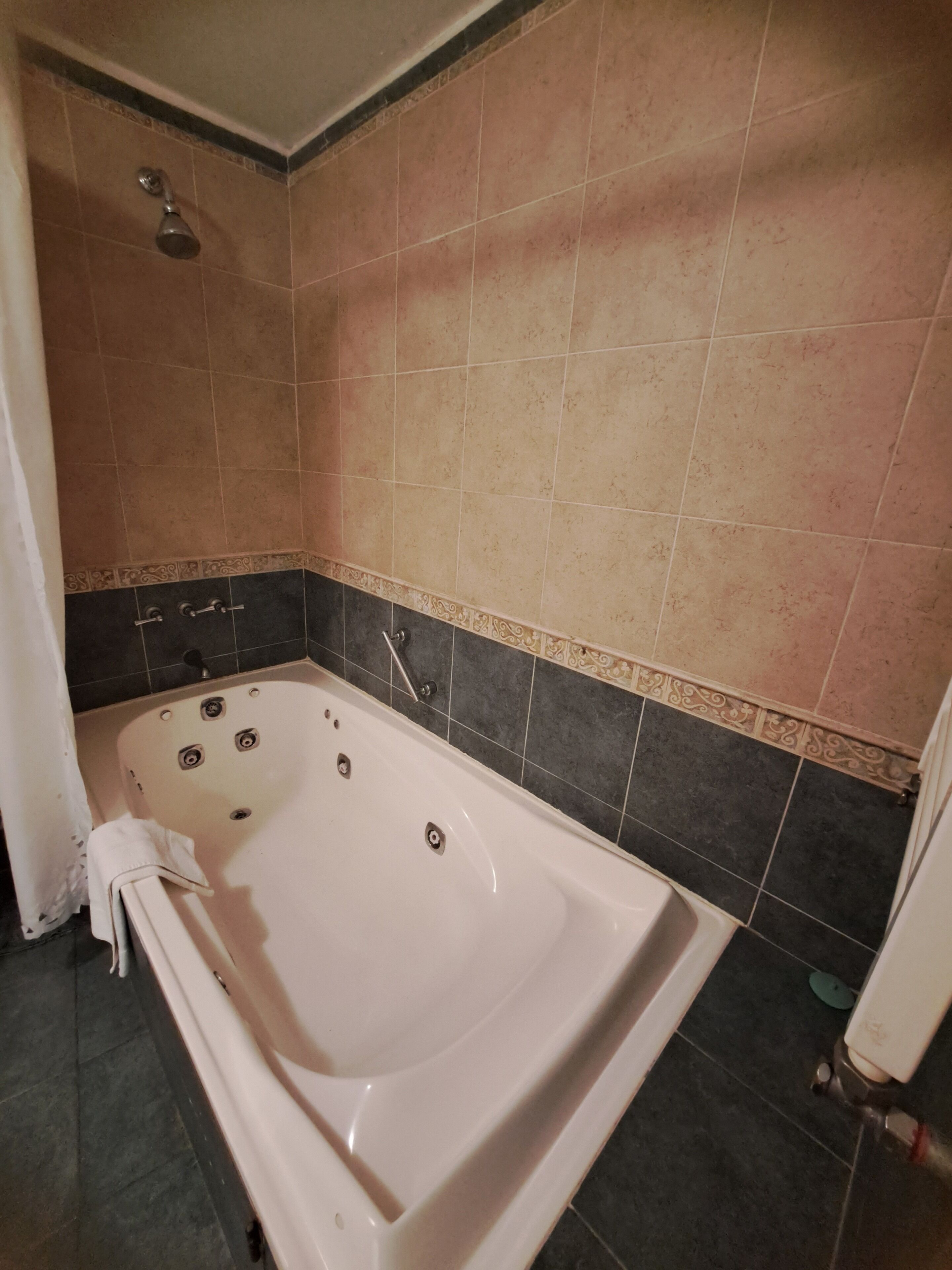 Un baño con bañera, azulejos oscuros y zona de ducha.