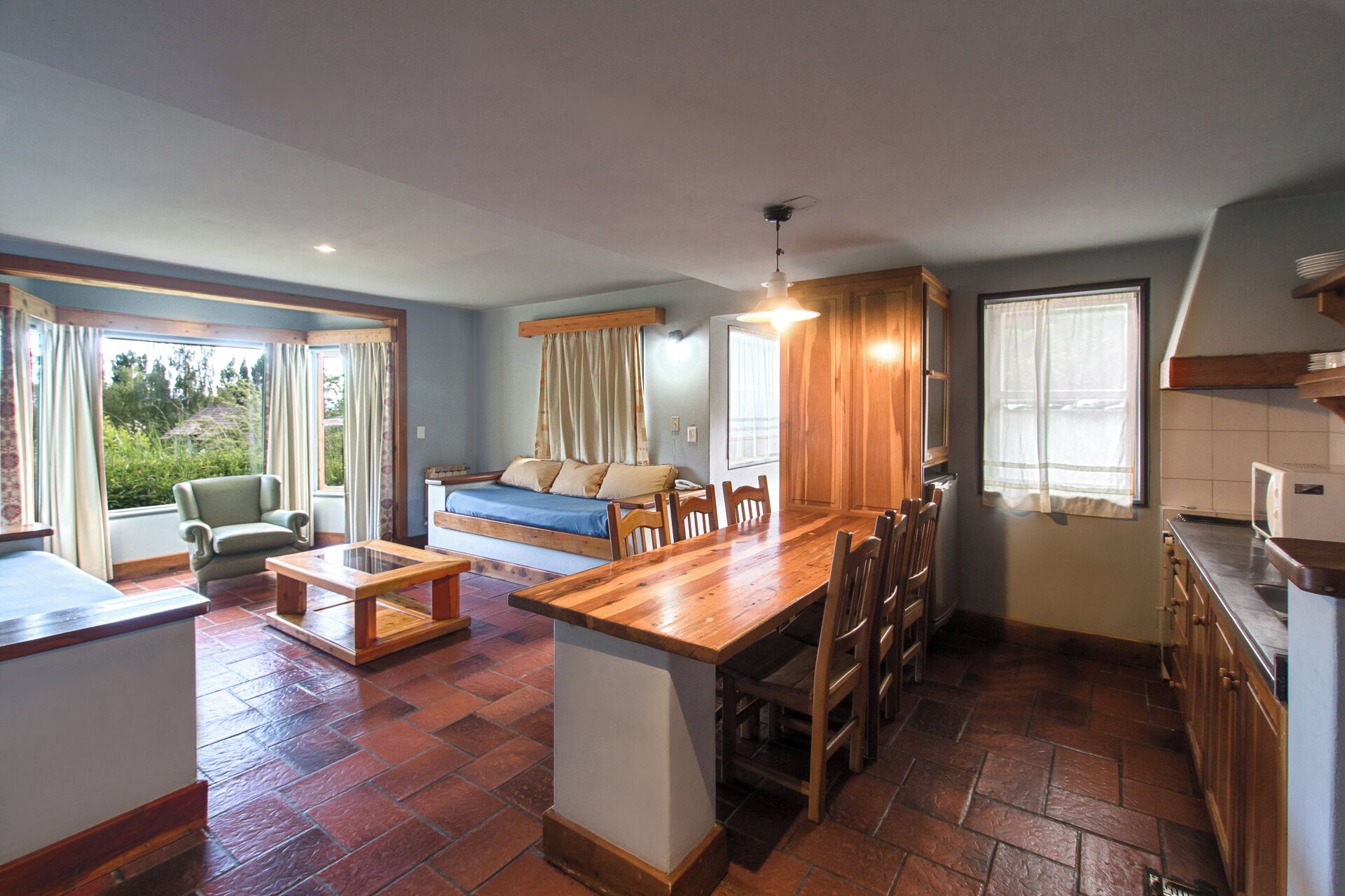 A cozy room with a wooden dining table, chairs, a sofa, and a kitchen area with a refrigerator and cabinets.