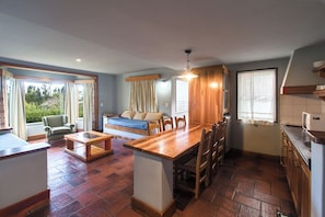 A cozy room with a wooden dining table, chairs, a sofa, and a kitchen area with a refrigerator and cabinets. - Rupu Pehuen Resort (San Carlos de Bariloche)