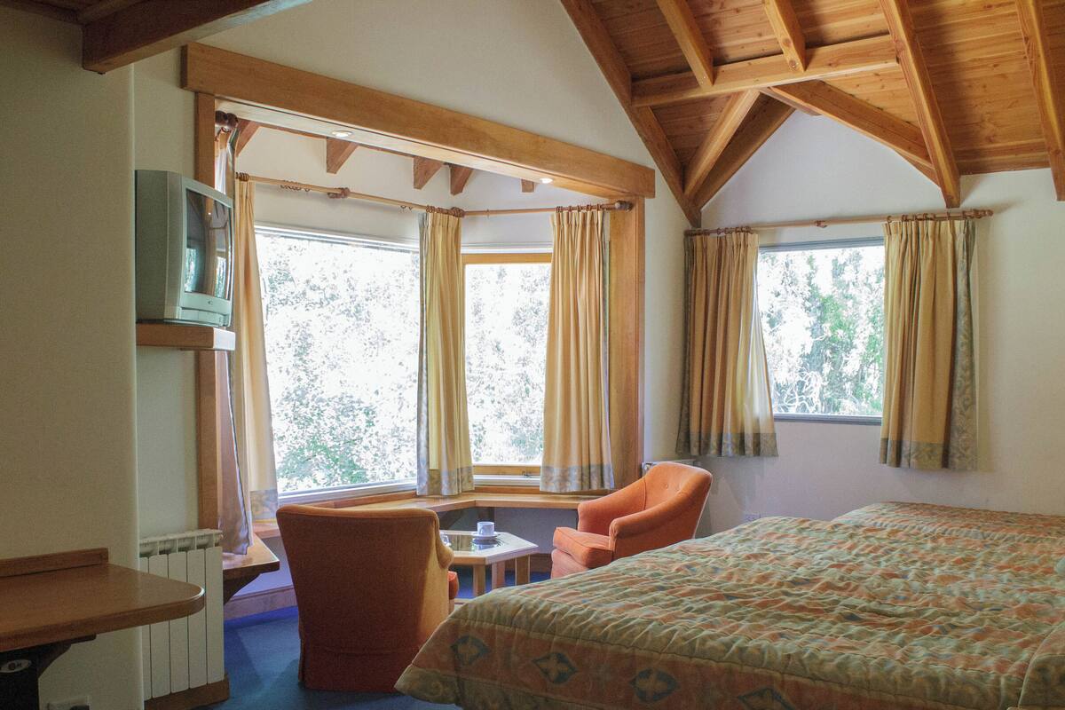 A room with a bed, a chair, a small table, and a window with curtains.