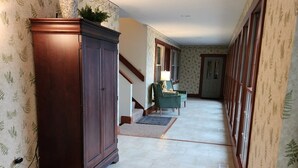 A hallway with patterned wallpaper, a wooden cabinet, a staircase, and a door at the end.