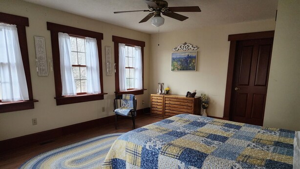 Une chambre à coucher avec un grand lit, une chaise, une commode et un ventilateur de plafond.