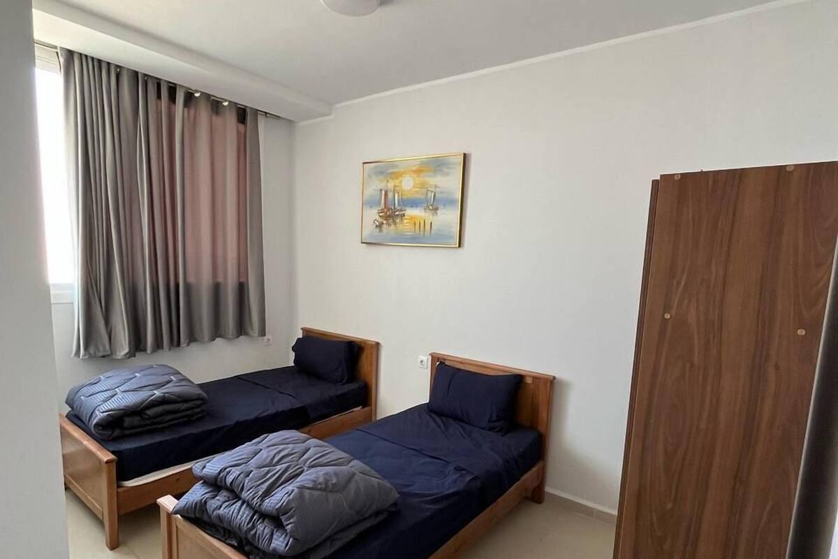 A room with two wooden beds, a painting on the wall, a window with curtains, and a wardrobe.