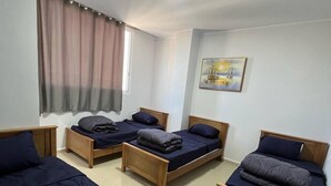 A dormitory room with four single beds, a window with curtains, a ceiling light, and a painting on the wall. - DORTOIR ADAM (Algiers)