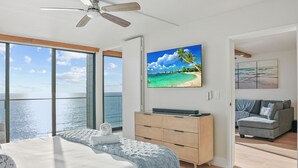 A modern bedroom with a large bed, a ceiling fan, and a view of the ocean through large windows. - Oceanfront Paradise with Sunset Balcony, Pool, Spa, Beach Access & Parking (San Diego)