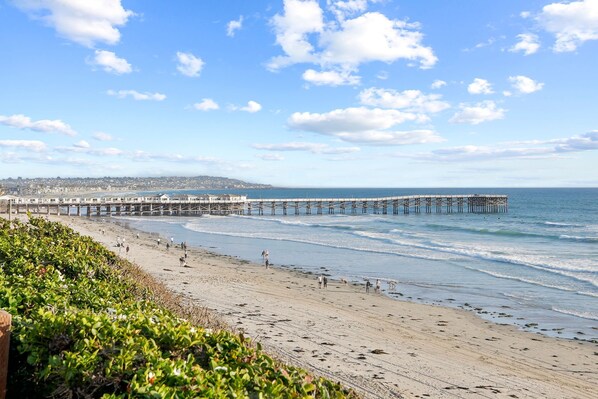 A beach with a pier extending into the water, a sandy shore, and a clear sky.
