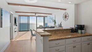 A modern kitchen with a granite countertop, white cabinetry, and a coffee maker. - Oceanfront Paradise with Sunset Balcony, Pool, Spa, Beach Access & Parking (San Diego)