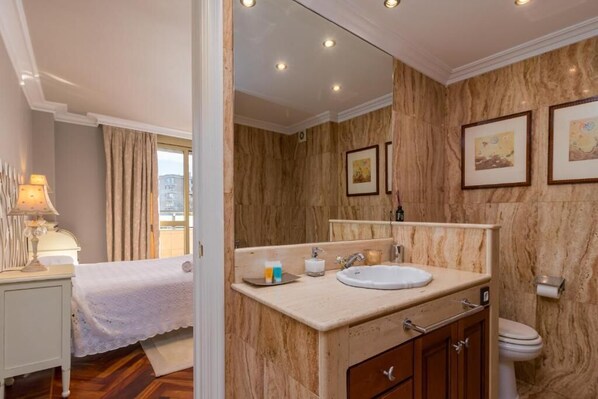 Une salle de bain d’hôtel avec un mur en marbre, un lavabo, un miroir et des toilettes.