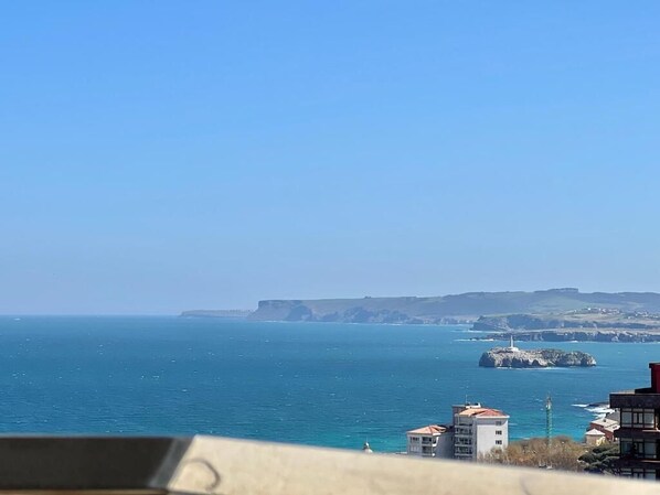 A coastal view with buildings near the water, a lighthouse, and cliffs in the distance. - Apartment Near Sardinero Beach with Parking (Santander)