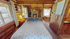 Ein Blockhaus-Zimmer mit Bett, Kamin, einer Karte an der Wand und einem Fenster mit Jalousien.