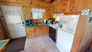 Eine kleine Küche mit Holzausstattung, einem Kühlschrank, einem Herd und einem Spülbecken.