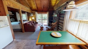 Ein gemütliches Blockhaushaus-Interieur mit Holzbalkendecke, einem grünen Tisch, einer Couch und einem Kamin.