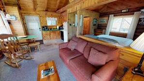 Ein gemütliches Blockhaus-Interieur mit einem Holzespeisetisch, einer Couch, einem Schaukelstuhl und einer Küchenzeile mit Kühlschrank und Spüle.