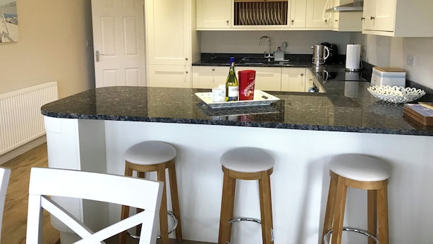A kitchen with white cabinets, a granite countertop, a coffee maker, and a paper towel dispenser. - Pen Y Frith Bungalow (Prestatyn)