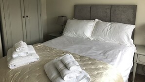 A neatly made bed with white linens and pillows, a bedside table with a lamp, and a wardrobe with two doors. - Pen Y Frith Bungalow (Prestatyn)