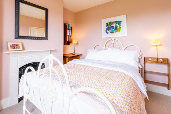 A bedroom with a white metal bed frame, a white fireplace, a bookshelf, and a painting on the wall. - Ocean View, Walberswick (Walberswick)