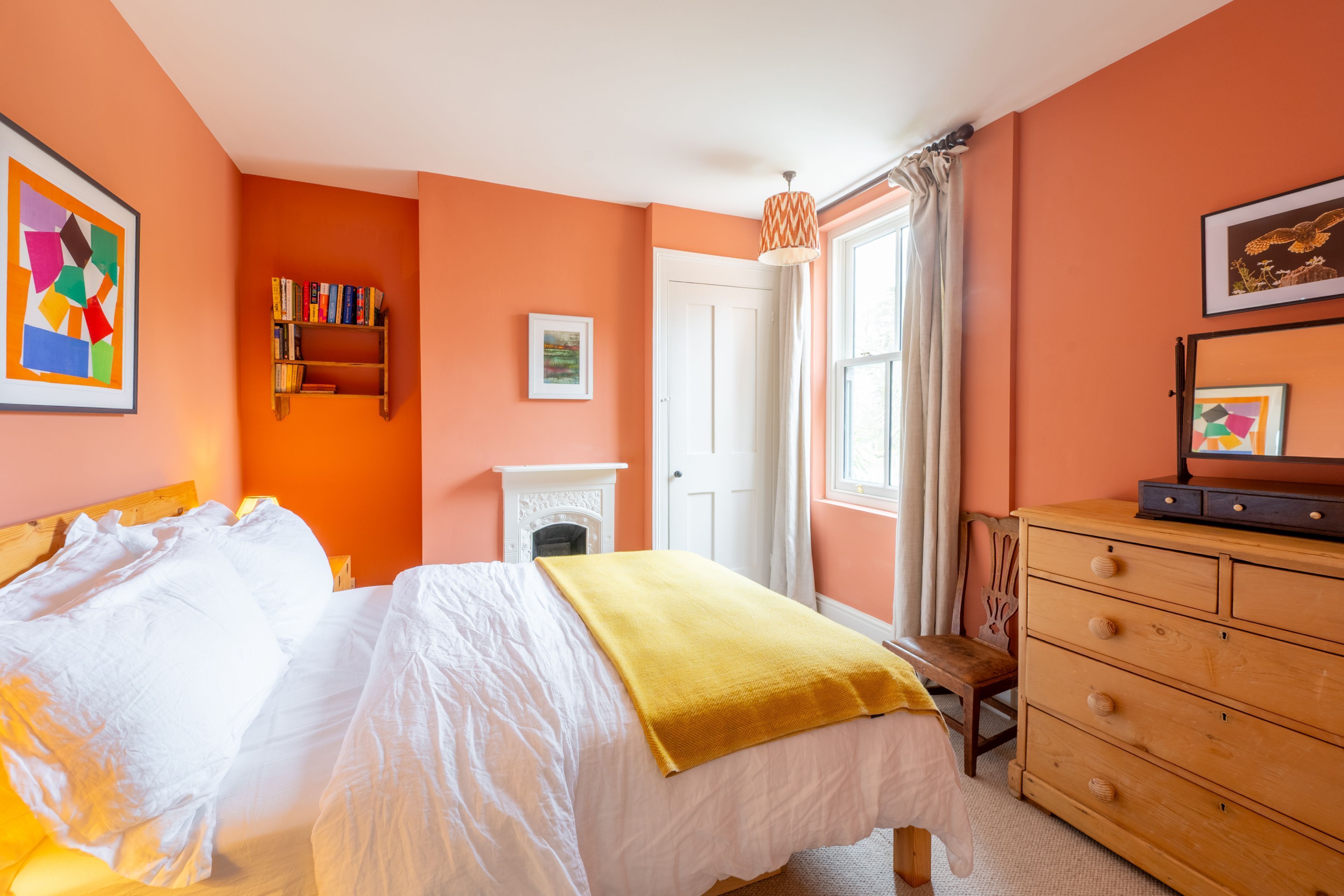 Een slaapkamer met een bed, een houten dressoir, een boekenkast en een open haard.