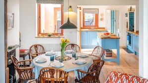 A dining area with a round table set for four, surrounded by wooden chairs. There is a vase with flowers on the table, and a hanging light fixture above. - Ocean View, Walberswick (Walberswick)