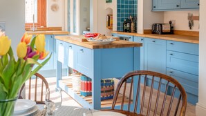 A kitchen with blue cabinets, a wooden island, and a dining area with chairs and a table. - Ocean View, Walberswick (Walberswick)