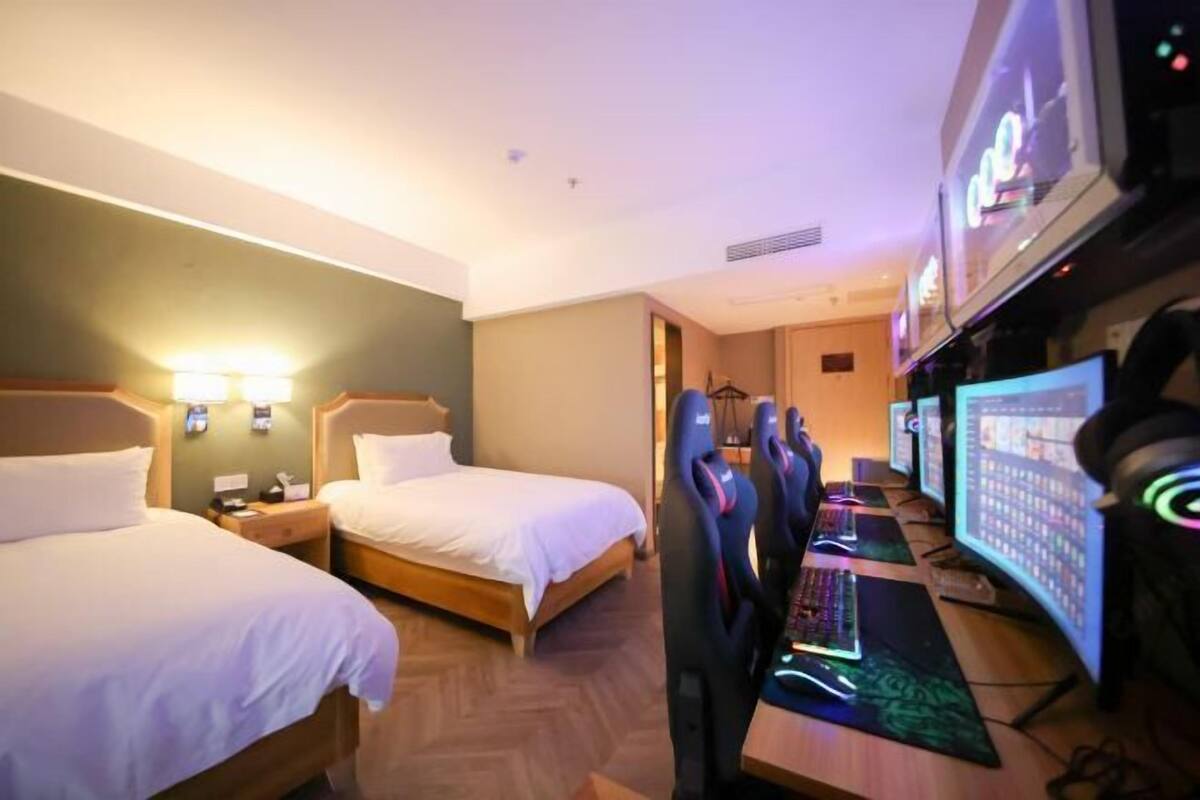 A hotel room with two beds, a desk with a computer and multiple monitors, and a television.