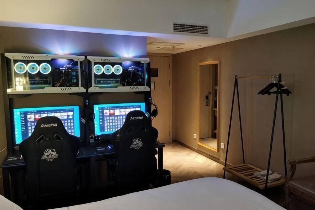 A hotel room with a gaming setup including two monitors, two gaming chairs, and a desk.