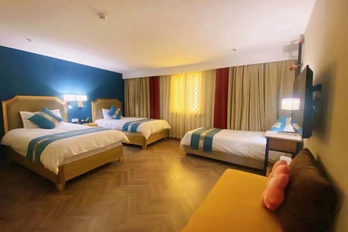 A hotel room with two single beds, a sofa, a TV, and a window with curtains.