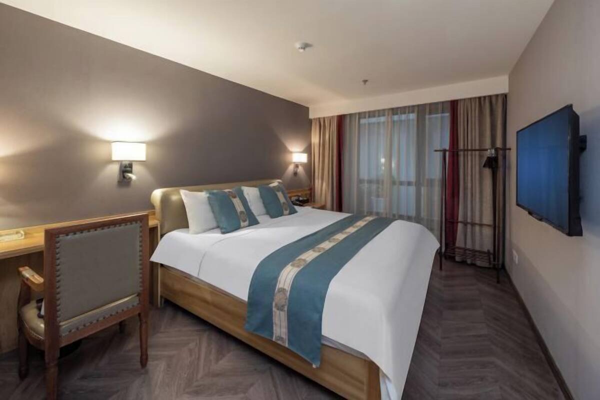 A hotel room with a large bed, a desk, and a television on the wall.