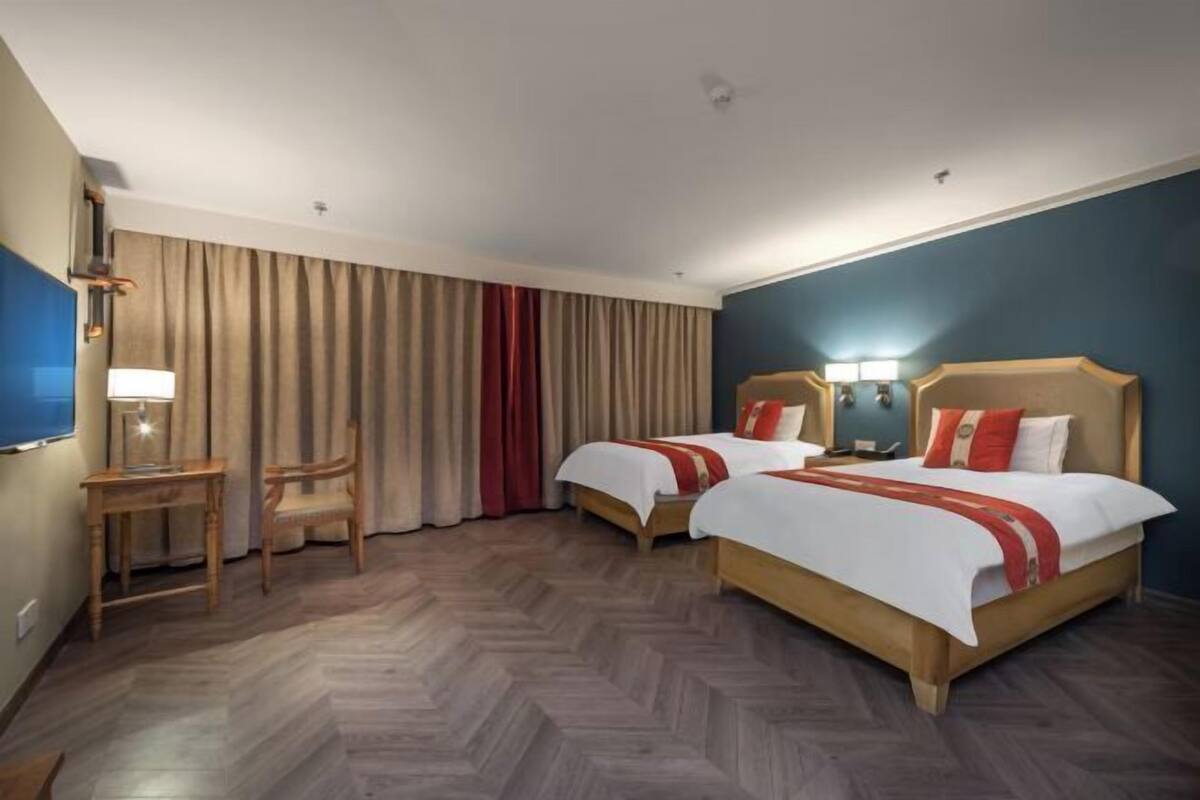 A hotel room with two beds, a desk, a chair, and a TV.