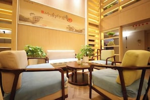 A hotel lobby with seating arrangements, a reception desk, and a wall with a decorative sign. - Grand Cozy Hotel (Nanjing University of the Arts Longjiang Subway Station Store) (Nanjing)