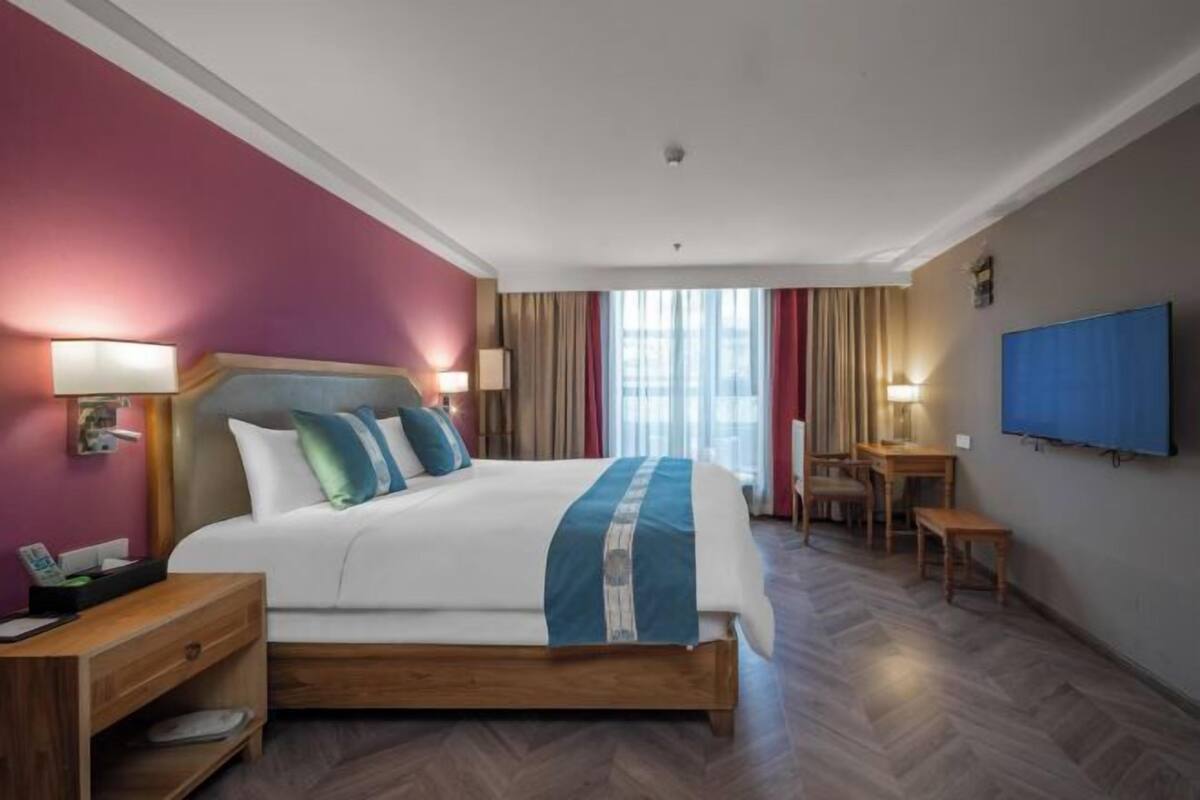A hotel room with a large bed, bedside tables, a desk, and a TV.