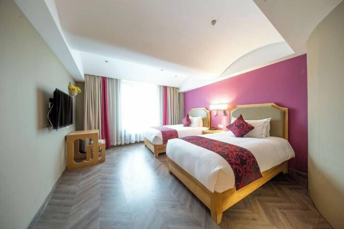 A hotel room with two beds, a TV, a bedside lamp, and a window with curtains.