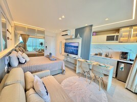 Quarto de hotel moderno com cama, área de estar, escrivaninha e cozinha compacta.