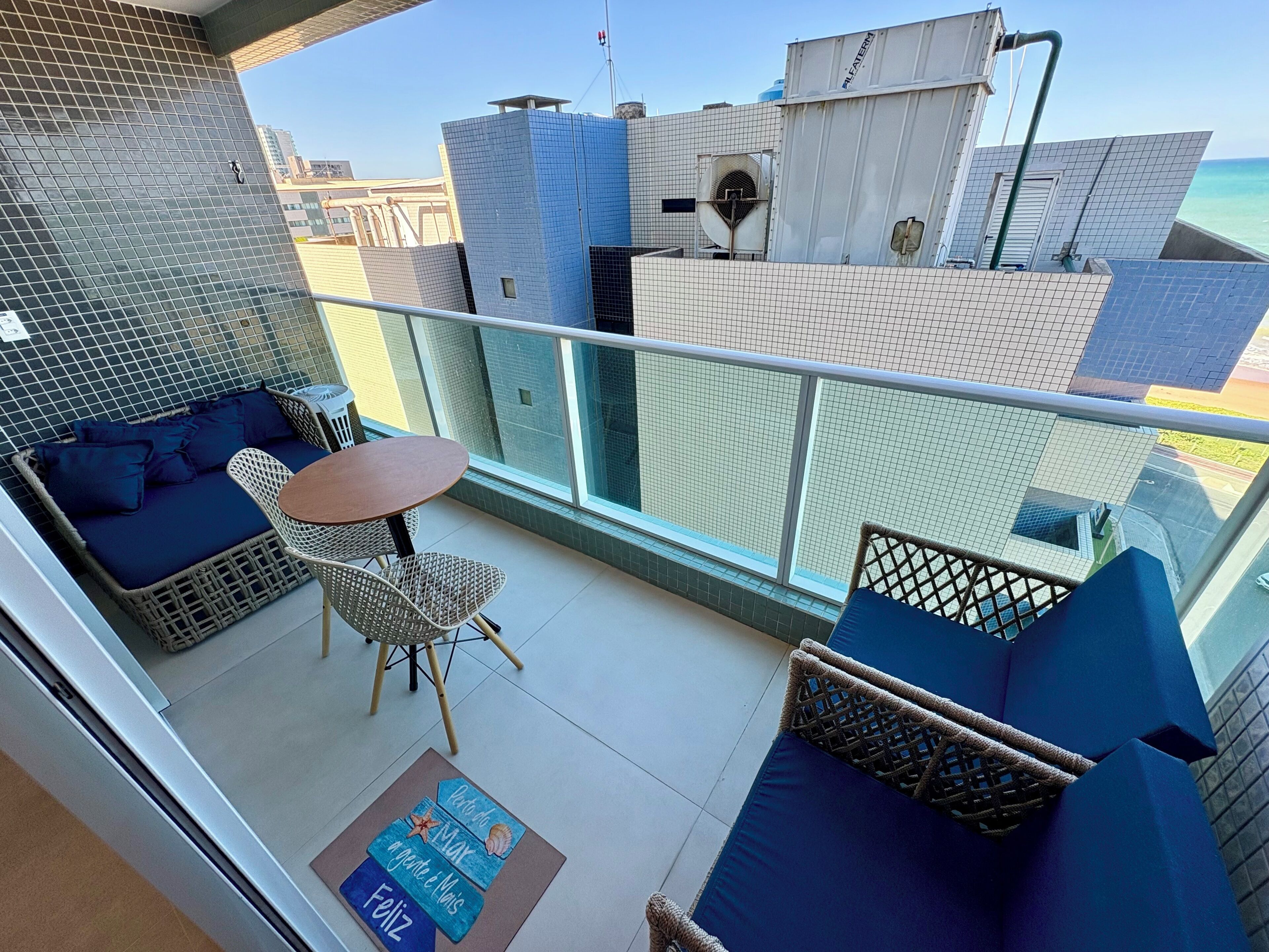 A balcony with a seating area, a table, and a view of the sea.
